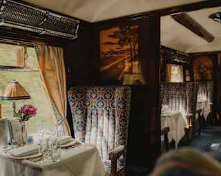 In Audrey, a luxurious blue-grey seat faces a table and abuts a partition wall with a marquetry depiction of a country scene.