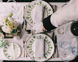 A waiter's gloved hand arranges cutlery between elegant Sultan's Garden crockery on a pretty dining table, seen from above.