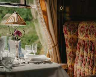 Soft window light falls on a dining table laid for guests and a padded, Art Deco beige and red chair, in a Gwen Car detail.