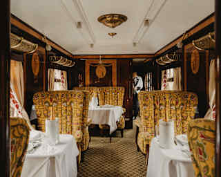 A steward approaches the Ibis Car where Champagne bottles await guests on three visible tables with seats in warm gold tones.