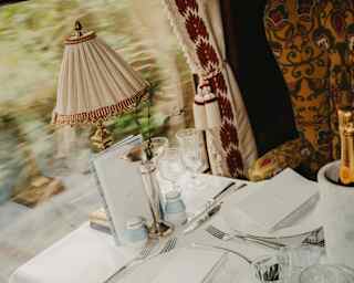 A view rushes past the window of an Ibis Car dining table, laid for two with a lamp and a Champagne cooler, seen from above.