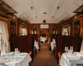 The Perseus Carriage, ready for diners with white-cloth tables and crystal glasses set between high-back russet velvet chairs.