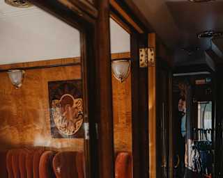View through the glass panels of a car door into the Perseus Carriage, capturing two high-back russet seats at a laid table.