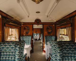 Teal and grey-patterned high-back seats flank white dining tables in a view through the wood-panelled Phoenix Carriage.