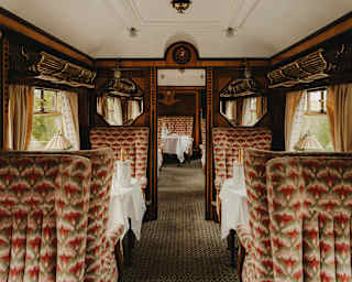 View through the Zena Car with dining tables and seats, upholstered in a grey and pink fabric, and wood panelled walls.