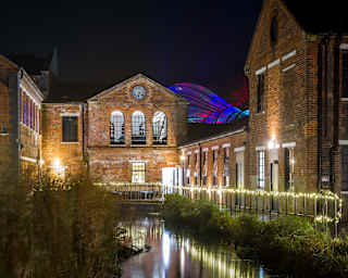 Night view of Laverstoke Mill, now the Bombay Sapphire Distillery, with its walkway fairy lights reflecting in the River Test.