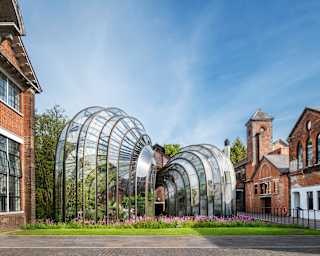 Two intertwined botanical glasshouses with a bulbous funnel design, set on lawned gardens between red-brick buildings.