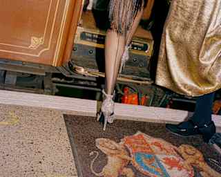 Low-angle image of a woman dressed in a black and gold sequin flapper dress, as she steps up into a car, seen from behind.