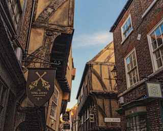 View of The Shambles in York where ancient beamed buildings lean, heads almost together, over a medieval cobbled lane.