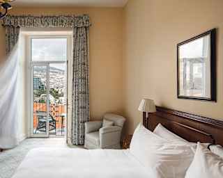 The hills of Madeira's capital, Funchal are seen through balcony doors on the other side of the bed in a Deluxe Sea View Room.