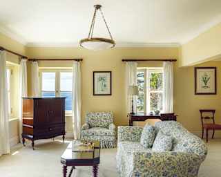 An elegant living area, furnished with antique wood pieces and a floral blue sofa suite facing sea view windows on two sides.