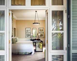 Looking from the Junior Suite Deluxe balcony into the bedroom, with warm wheat-toned wallpaper and fresh white bed linen.