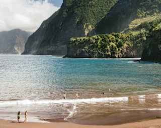 Lush coastal mountains dive into the blue waters at Seixal Beach, where the black sand looks momentarily golden in the sun.