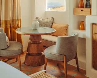 A round table with conical pedestal and two soft chairs bathes in light from an arched window in the wall above a banquette.