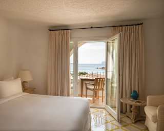 Looking over an immaculate white double bed to the balcony doors, which open onto a seating area with sublime ocean views.