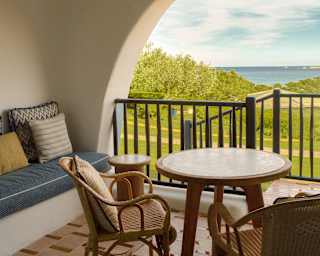 A blue sofa, two tables and a pair of cane chairs, claim lush coast views from a recessed balcony with steps down to the garden.