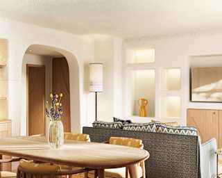 View over a wooden dining table, by stocked bottle shelves, to a living space with a sofa facing a wall of alcoves and tv.