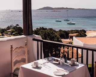 An al-fresco table for two sits in the corner of La Terrasse restaurant, with a view of three boats floating in the blue sea.