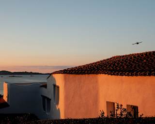 Late sun turns the white rendering of a Romazzino residence rose-gold in an image that captures the sea and a soaring bird.