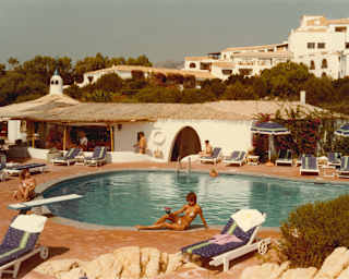 Historic honeyed Kodachrome photo of guests lounging with drinks by the sun-drenched resort pool, with a thatched bar area.