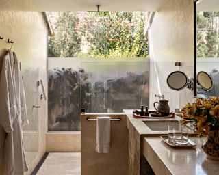View into a Garden Junior Suite marble galley bathroom with a basin unit and light-filled monsoon shower with glass ceiling.
