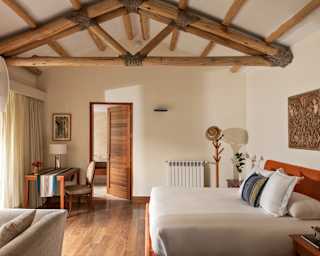 View of a Garden Junior Suite with pristine bed, desk and hat stand in a room with abundant wood in beams, floors and doors.