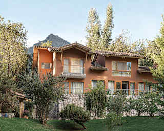 The large Villa Q'inti, with terracotta exterior, rises from a garden of lawns and ancient trees on a stone supporting wall.