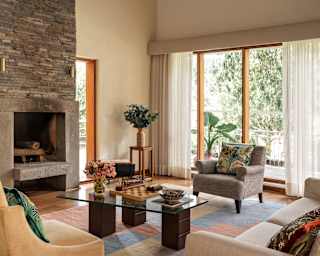A sofa and two armchairs circle a rhombus glass-top table in the spacious living room, with a fireplace and window walls.