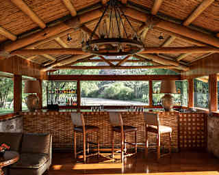 Beneath a wood-beamed roof, three high-back stools sit along the bar at El Huerto Bar with a direct view to the Urubamba River.