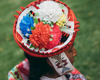 A local woman wears a montera hat with a thick chin strap and red, white and blue paper flower decorations, seen from above.