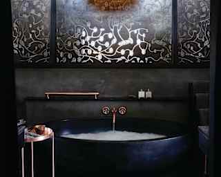 Curved ebony bathtub with rose gold taps and black slate wall tiles