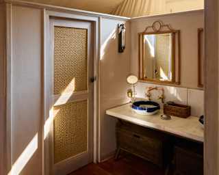 A shaft of sunlight from a high window falls across a cubicle door in a bathroom with a pendant light and marble vanity.