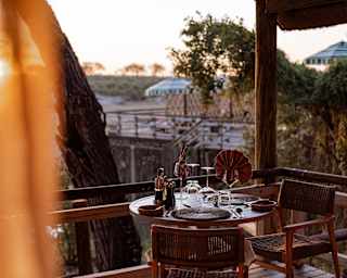 A laid table for two, with fanned napkins in wineglasses, awaits diners on a dining deck, as late sun glows on the horizon.