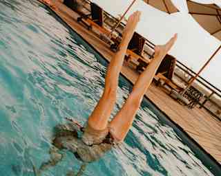 Angled image of a woman performing a handstand in the pool, with only her legs emerging from the water.