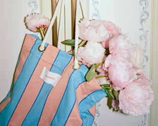 Stems of soft pink peonies fill a blue and pink-stripe tote bag which hangs from one of a pair of gold-tone cupboard handles.
