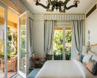 A Premium Room, with a double bed and décor in subdued Regency pastels, bathes in light from double glass doors on two sides.