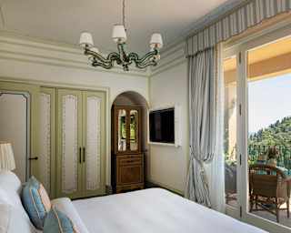 Internal view over crisp white bedlinen and through terrace doors to a dazzling vista of green hills and sparkling blue bay.
