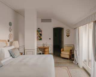 Three decorative plates and an artwork hang on the fresh white walls of the Portofino Suite, viewed across a wide bed.