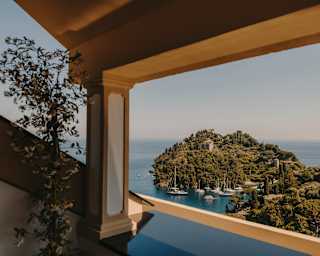 Boats float in the blue waters around the verdant Punta del Coppo, seen from the covered terrace of a Portofino Suite.