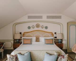 A sofa with blue and floral cushions abuts a Junior Suite bed with ornamental wall plates above and flanked by side tables.