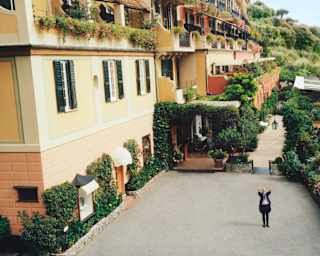 The concierge waves from the hotel's courtyard, surrounded by lush wall-hugging ivy and a long hedge of pink roses