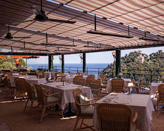 Two rows of tables with rattan chairs keep cool beneath a terracotta and white striped terrace canopy at Splendido Grill.