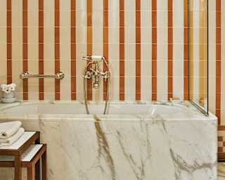 Carrara marble bath under terracotta striped tiles in a luxurious bathroom
