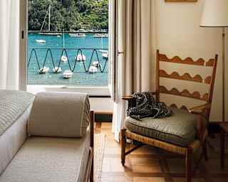 Suite interior with a chair and an open window with a view of boats on Portofino Bay