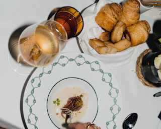 Looking down on a dining table as a guest enjoys a meal with wine, water and a basket of breads, at Dav Mare restaurant.