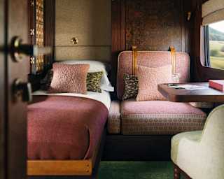 View into a double cabin with one fold-down bed made with white sheets and burgundy blanket, and the other in chair position.