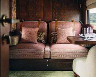Two dusty-pink seats sit against the wood-panelled wall in a cabin with a table set with wine in a cooler and two glasses.