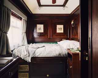 View through a Double Cabin to an unmade bed with white bedding, bathed in window light and encased in dark wood panelling.