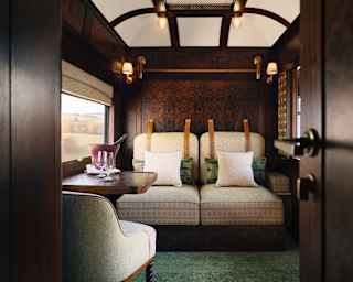 Two cream fold-down beds sit in chair position against the wood panelling, seen in a luxurious green-carpeted cabin.