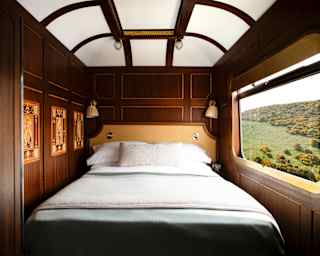 A bed nestles between a wood wall with three marquetry panels and a window onto verdant hills in the Grand Suite bedroom.